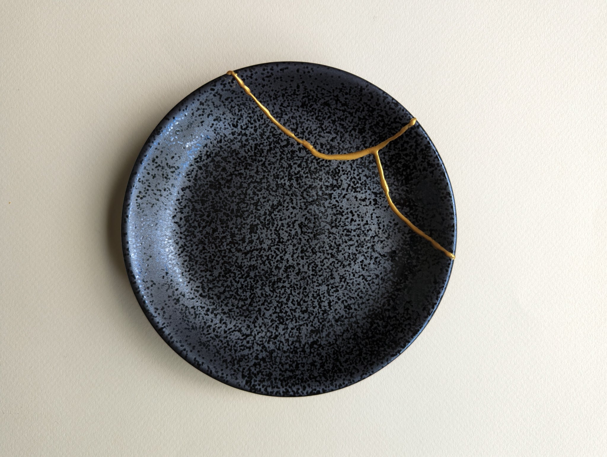 small black saucer repaired using mended with gold kintsugi ceramic repair kit